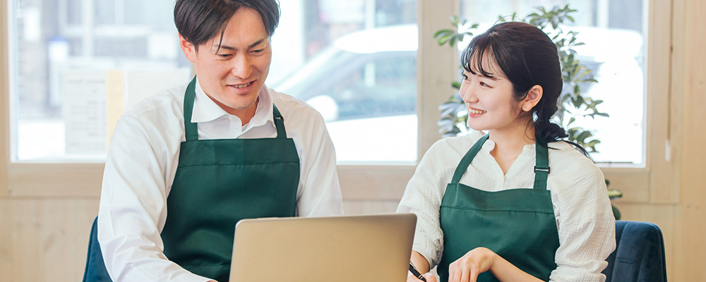 パソコンの前で会話している飲食店スタッフ2名