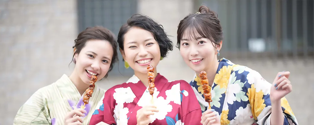 お祭りで焼き鳥を買った浴衣を着た女性3人