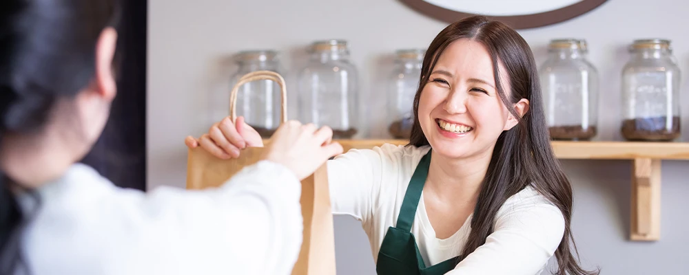 カフェで笑顔で紙袋を手渡すエプロン姿の女性店員